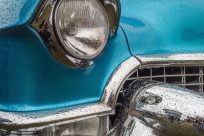 A closeup shot of the front part of a blue car including the lights and the bumper